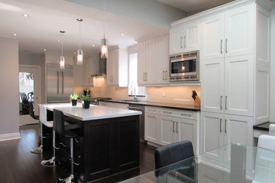 Enclosed kitchen - large transitional l-shaped dark wood floor enclosed kitchen idea in Toronto with an undermount sink, shaker cabinets, white cabinets, quartz countertops, white backsplash, stone slab backsplash, stainless steel appliances and an island