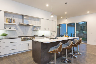 This is an example of a large open plan kitchen in Austin with a double-bowl sink, white cabinets, white splashback, stainless steel appliances, medium hardwood flooring, an island, brown floors, white worktops, engineered stone countertops and porcelain splashback.
