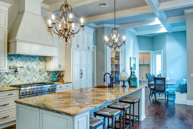 Example of a large transitional l-shaped dark wood floor and brown floor open concept kitchen design in Orlando with a farmhouse sink, raised-panel cabinets, white cabinets, granite countertops, blue backsplash, stone tile backsplash, paneled appliances and an island