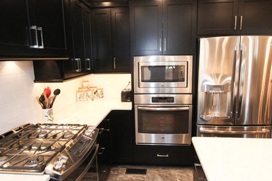 Example of a mid-sized classic vinyl floor kitchen design in Other with flat-panel cabinets, black cabinets, quartzite countertops, white backsplash, ceramic backsplash, stainless steel appliances and an island