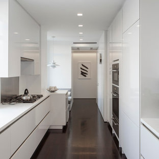Foto de cocina comedor de galera, actual, de tamaño medio, con armarios con paneles con relieve, puertas de armario blancas, salpicadero beige, electrodomésticos de acero inoxidable y suelo de madera oscura