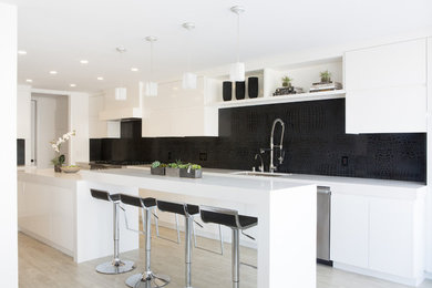 Inspiration for a large modern eat-in kitchen remodel in Los Angeles with an undermount sink, flat-panel cabinets, white cabinets, quartz countertops, black backsplash, stone slab backsplash and stainless steel appliances