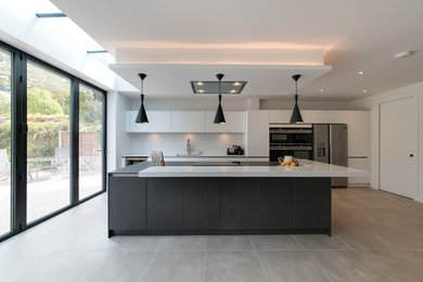 Design ideas for a medium sized contemporary single-wall enclosed kitchen in London with a submerged sink, flat-panel cabinets, white cabinets, quartz worktops, white splashback, an island and grey floors.