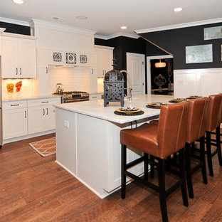 Imagen de cocina de galera, clásica renovada, grande, abierta, con armarios con paneles empotrados, puertas de armario blancas, salpicadero blanco, salpicadero de azulejos tipo metro, electrodomésticos de acero inoxidable, encimera de mármol, suelo de madera en tonos medios y una isla
