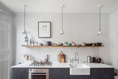 Inspiration for a small traditional kitchen/diner in London with a belfast sink, flat-panel cabinets, black cabinets, quartz worktops, white splashback, integrated appliances, dark hardwood flooring and an island.