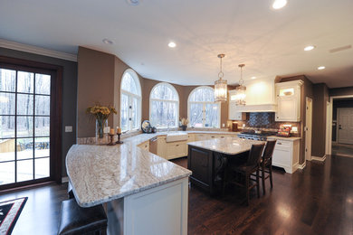 Example of a large transitional u-shaped dark wood floor eat-in kitchen design in Cleveland with white cabinets, an island, a farmhouse sink, granite countertops, brown backsplash, subway tile backsplash, stainless steel appliances and recessed-panel cabinets