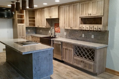 Mid-sized transitional l-shaped medium tone wood floor and beige floor kitchen photo in Tampa with a farmhouse sink, recessed-panel cabinets, medium tone wood cabinets, soapstone countertops, gray backsplash, stone slab backsplash, stainless steel appliances and an island