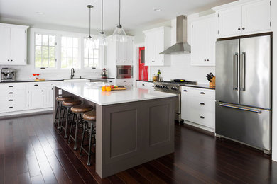 Example of a large beach style l-shaped dark wood floor and brown floor eat-in kitchen design in Seattle with a farmhouse sink, shaker cabinets, white cabinets, quartzite countertops, white backsplash, ceramic backsplash, stainless steel appliances and an island