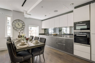 Photo of a contemporary single-wall open plan kitchen in London with flat-panel cabinets, composite countertops, mirror splashback, black appliances, medium hardwood flooring, no island, brown floors and grey worktops.