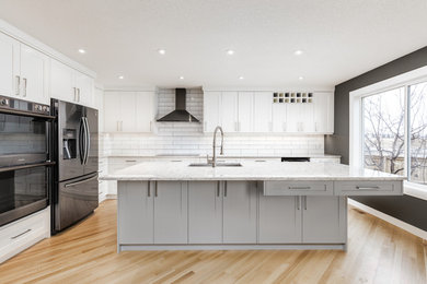 Inspiration for a transitional l-shaped light wood floor and beige floor kitchen remodel in Calgary with an undermount sink, shaker cabinets, white cabinets, white backsplash, subway tile backsplash, an island and gray countertops