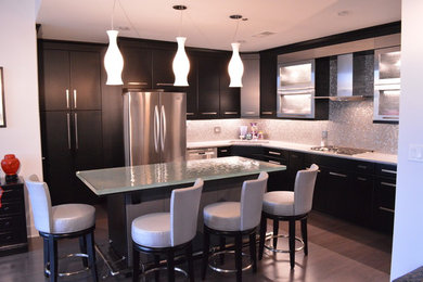 Eat-in kitchen - contemporary l-shaped eat-in kitchen idea in Raleigh with flat-panel cabinets, black cabinets, glass countertops, metallic backsplash, stainless steel appliances and an island