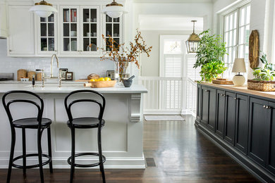 Open concept kitchen - mid-sized transitional u-shaped dark wood floor and brown floor open concept kitchen idea in Raleigh with a farmhouse sink, glass-front cabinets, white cabinets, quartz countertops, white backsplash, subway tile backsplash, an island and white countertops