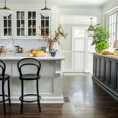 Open concept kitchen - mid-sized transitional u-shaped dark wood floor and brown floor open concept kitchen idea in Raleigh with a farmhouse sink, glass-front cabinets, white cabinets, quartz countertops, white backsplash, subway tile backsplash, an island and white countertops