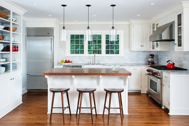 Transitional l-shaped kitchen photo in New York with stainless steel appliances, stone tile backsplash, wood countertops, shaker cabinets, white cabinets and white backsplash
