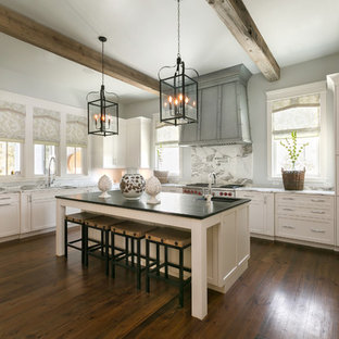 Imagen de cocina en L, clásica renovada, abierta, con armarios estilo shaker, puertas de armario blancas, salpicadero blanco, salpicadero de losas de piedra, electrodomésticos de acero inoxidable, suelo de madera oscura, una isla, fregadero encastrado y encimera de mármol