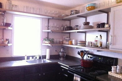 Exempel på ett litet industriellt kök, med en enkel diskho, svarta skåp, stänkskydd i tunnelbanekakel, svarta vitvaror och en köksö