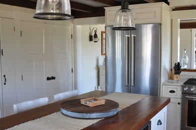 Example of a mid-sized beach style l-shaped medium tone wood floor and beige floor enclosed kitchen design in Providence with a farmhouse sink, recessed-panel cabinets, white cabinets, granite countertops, gray backsplash, wood backsplash, stainless steel appliances and an island