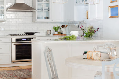 Eat-in kitchen - mid-sized transitional u-shaped light wood floor eat-in kitchen idea in Boston with a farmhouse sink, recessed-panel cabinets, white cabinets, marble countertops, white backsplash, ceramic backsplash, paneled appliances, a peninsula and white countertops