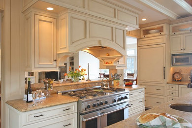 Example of a large classic l-shaped medium tone wood floor open concept kitchen design in New York with recessed-panel cabinets, white cabinets, granite countertops, stone tile backsplash, paneled appliances, an undermount sink and beige backsplash