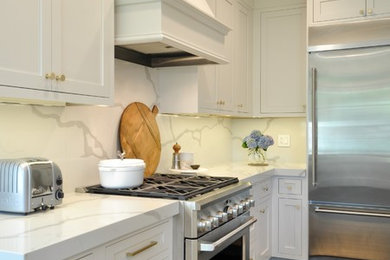 Diseño de cocina clásica renovada con salpicadero blanco, electrodomésticos de acero inoxidable, una isla y encimeras blancas