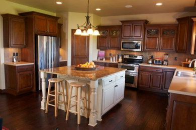 Inredning av ett klassiskt mellanstort kök, med en dubbel diskho, luckor med upphöjd panel, skåp i mellenmörkt trä, granitbänkskiva, flerfärgad stänkskydd, stänkskydd i keramik, rostfria vitvaror, mörkt trägolv och en köksö