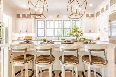 Example of a large farmhouse u-shaped light wood floor and brown floor eat-in kitchen design in Atlanta with a farmhouse sink, beaded inset cabinets, white cabinets, marble countertops, white backsplash, wood backsplash, stainless steel appliances, an island and gray countertops
