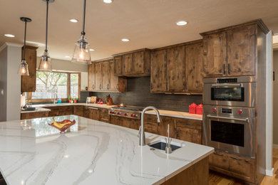 Example of a large classic l-shaped medium tone wood floor and brown floor open concept kitchen design in Dallas with an undermount sink, flat-panel cabinets, dark wood cabinets, quartz countertops, black backsplash, porcelain backsplash, stainless steel appliances, an island and white countertops