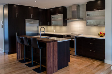 Example of a mid-sized trendy l-shaped medium tone wood floor and brown floor open concept kitchen design in Montreal with an undermount sink, shaker cabinets, dark wood cabinets, quartz countertops, gray backsplash, glass tile backsplash, stainless steel appliances and an island