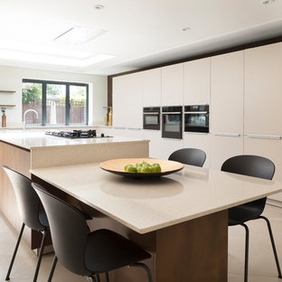 Large contemporary l-shaped kitchen/diner in London with an integrated sink, flat-panel cabinets, beige cabinets, quartz worktops, beige splashback, stone slab splashback, black appliances, porcelain flooring, an island, beige floors and beige worktops.