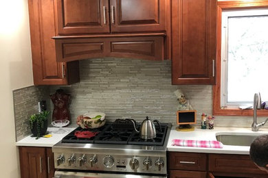 Example of a mid-sized classic l-shaped ceramic tile and white floor kitchen pantry design in New York with an undermount sink, raised-panel cabinets, medium tone wood cabinets, quartz countertops, gray backsplash, glass tile backsplash, stainless steel appliances, no island and white countertops