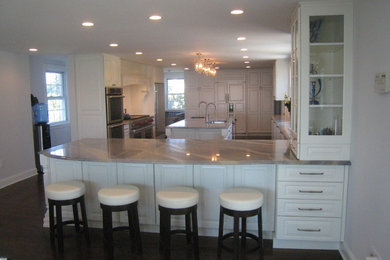 Large elegant l-shaped dark wood floor enclosed kitchen photo in New York with an undermount sink, raised-panel cabinets, white cabinets, granite countertops, white backsplash, stainless steel appliances and an island