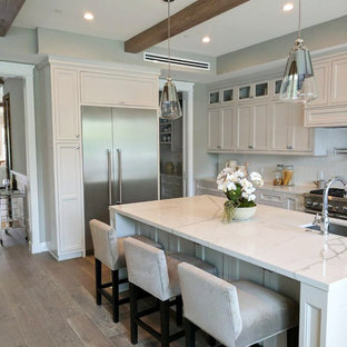 Large modern u-shaped eat-in kitchen in San Francisco with an integrated sink, louvered cabinets, white cabinets, marble benchtops, white splashback, stainless steel appliances, light hardwood floors, with island, grey floor, white benchtop and porcelain splashback.