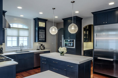 Klassisk inredning av ett mellanstort kök, med en enkel diskho, blå skåp, marmorbänkskiva, vitt stänkskydd, stänkskydd i tunnelbanekakel, rostfria vitvaror, mellanmörkt trägolv och en köksö