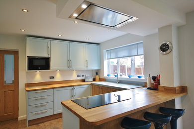 This is an example of a large contemporary open plan kitchen in Essex with an integrated sink, shaker cabinets, blue cabinets, wood worktops and black appliances.