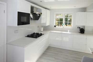 Moderne Wohnküche ohne Insel in L-Form mit weißen Schränken, Quarzit-Arbeitsplatte, Küchenrückwand in Weiß, schwarzen Elektrogeräten und weißer Arbeitsplatte in Essex