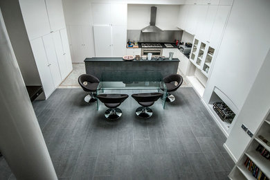 Photo of a large contemporary u-shaped open plan kitchen in London with flat-panel cabinets, white cabinets, granite worktops, metallic splashback, an island and black worktops.
