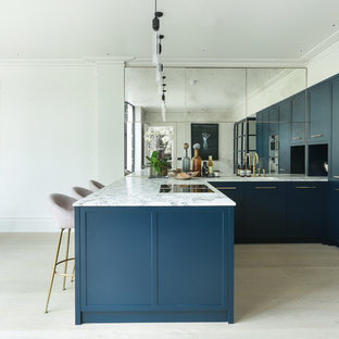 Inspiration for a contemporary u-shaped kitchen/diner in London with a submerged sink, shaker cabinets, blue cabinets, metallic splashback, mirror splashback, stainless steel appliances, light hardwood flooring, a breakfast bar, beige floors and white worktops.
