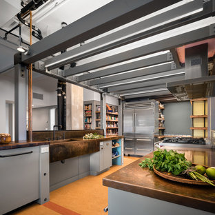 Large industrial galley separate kitchen in New York with an integrated sink, flat-panel cabinets, grey cabinets, copper benchtops, stainless steel appliances, cork floors, no island and brown floor.