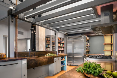 Large industrial galley kitchen in New York with an integrated sink, flat-panel cabinets, grey cabinets, copper worktops, stainless steel appliances, cork flooring, brown floors and an island.