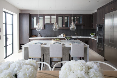 This is an example of a classic l-shaped kitchen/diner in London with a submerged sink, flat-panel cabinets, dark wood cabinets, grey splashback, mosaic tiled splashback, stainless steel appliances, an island, beige floors and white worktops.