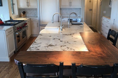 Kitchen - mid-sized transitional u-shaped medium tone wood floor kitchen idea in Denver with raised-panel cabinets, white cabinets, marble countertops, an island, a farmhouse sink, white backsplash, stone tile backsplash and paneled appliances