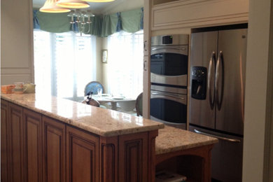Exemple d'une cuisine américaine chic en bois brun de taille moyenne avec un placard avec porte à panneau surélevé, un plan de travail en granite, un électroménager en acier inoxydable et parquet foncé.