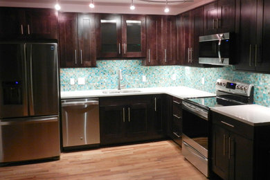 Kleine Moderne Küche in L-Form mit Unterbauwaschbecken, Schrankfronten im Shaker-Stil, dunklen Holzschränken, Quarzwerkstein-Arbeitsplatte, bunter Rückwand, Glasrückwand, Küchengeräten aus Edelstahl und hellem Holzboden in Denver