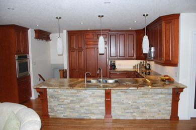 Mid-sized elegant u-shaped medium tone wood floor and brown floor kitchen photo in Toronto with an undermount sink, raised-panel cabinets, medium tone wood cabinets, granite countertops, paneled appliances, a peninsula and multicolored countertops