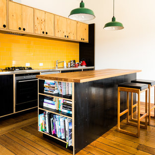 This is an example of a contemporary galley kitchen in Hobart with a drop-in sink, flat-panel cabinets, black cabinets, yellow splashback, subway tile splashback, stainless steel appliances, medium hardwood floors and with island.