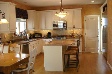 Mid-sized transitional l-shaped medium tone wood floor eat-in kitchen photo in Philadelphia with an undermount sink, raised-panel cabinets, white cabinets, granite countertops, beige backsplash, glass tile backsplash, stainless steel appliances and an island
