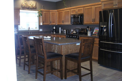 Eat-in kitchen - mid-sized craftsman l-shaped vinyl floor and gray floor eat-in kitchen idea in Milwaukee with an undermount sink, flat-panel cabinets, light wood cabinets, quartz countertops, black appliances, an island and multicolored countertops
