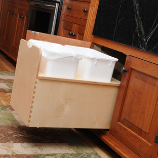 Inspiration for a mid-sized country l-shaped eat-in kitchen in Columbus with an integrated sink, raised-panel cabinets, medium wood cabinets, soapstone benchtops, beige splashback, stone tile splashback, stainless steel appliances, light hardwood floors and no island.
