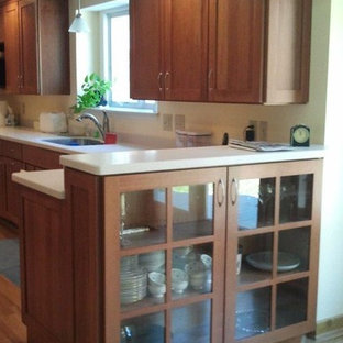 Example of a mid-sized cottage l-shaped medium tone wood floor eat-in kitchen design in New York with an undermount sink, shaker cabinets, medium tone wood cabinets, solid surface countertops, black appliances and a peninsula