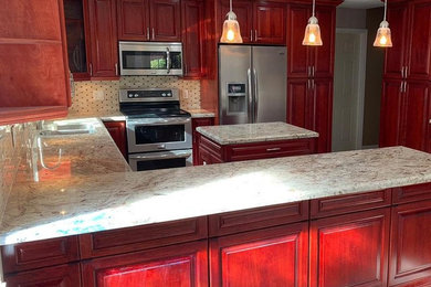 マイアミにあるコンテンポラリースタイルのおしゃれなキッチン (赤いキャビネット、御影石カウンター、ベージュキッチンパネル、シルバーの調理設備) の写真
